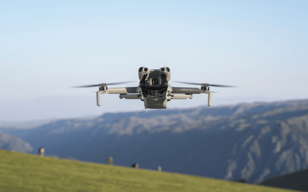 Auf dem Foto ist eine Mini 5 Pro zu sehen, die vor einer Gebirgskette fliegt.