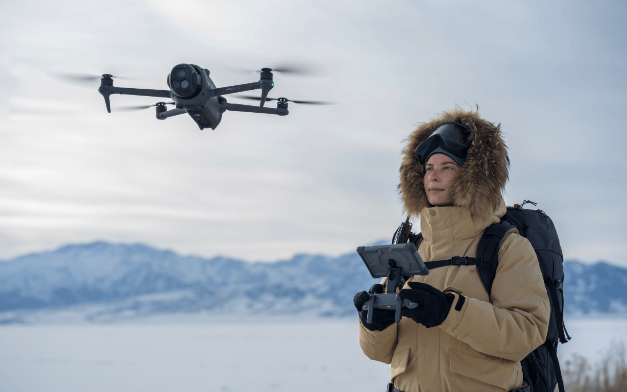 Auf dem Foto ist die DJI Mavic 4 Pro in einer Schneelandschaft zu sehen. Sie wird von einer Pilotin mit dem DJI RC Pro 2 Controller gesteuert. 