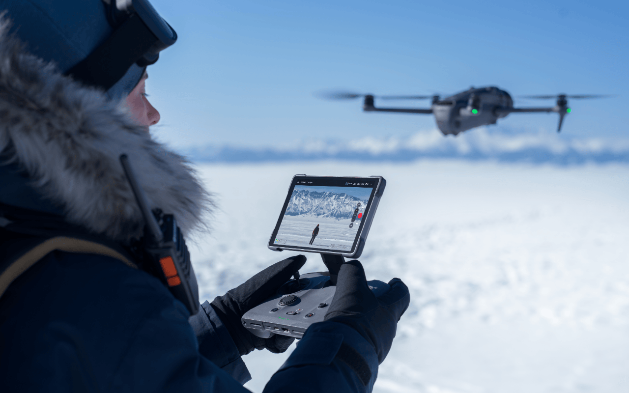 Auf dem Foto ist die DJI Mavic 4 Pro in einer Schneelandschaft zu sehen. Sie wird von einem Piloten mit dem DJI RC Pro 2 Controller gesteuert. 