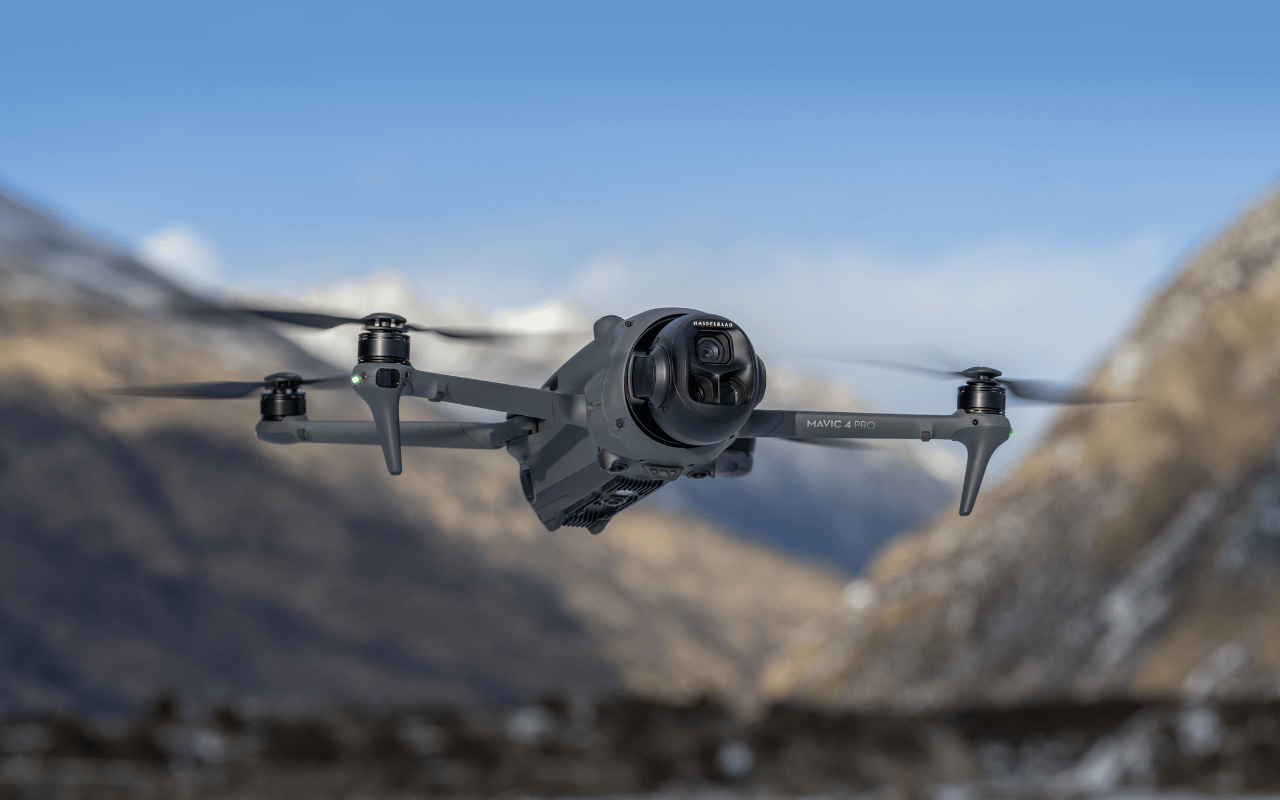 Auf dem Foto ist die fliegende  DJI Mavic 4 Pro, mit Bergen im Hintergrund, zu sehen.