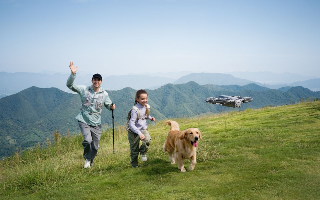 Auf dem Foto ist ein Mann und ein Mädchen zusehen. Zusammen mit ihrem Hund wandern sie durch die Berge. Die DJI Neo 2 filmt die Wanderer während der Wanderung. 