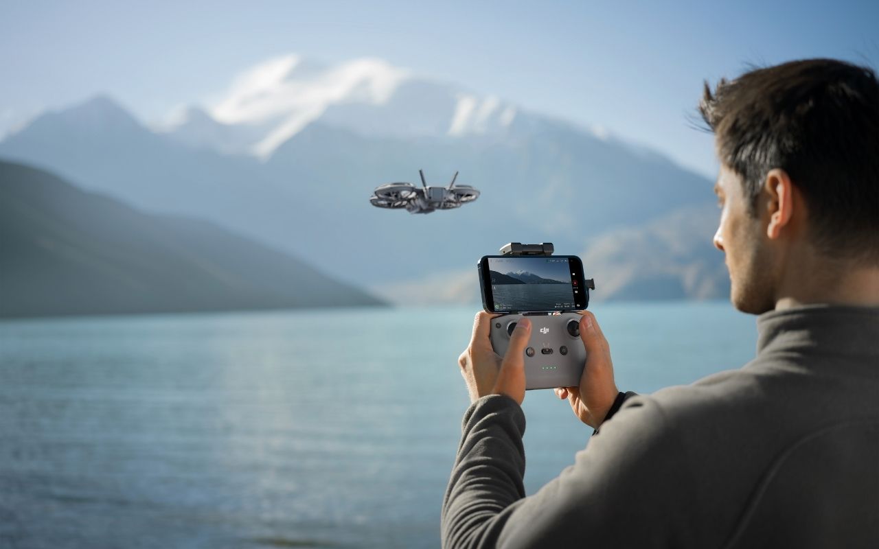 Auf dem Foto ist eine fliegende DJI Neo 2 Drohne im Hintergrund  und der Pilot im Vordergrund zu sehen. Der Pilot hält einen DJI RC-N3 Controller in der Hand. 